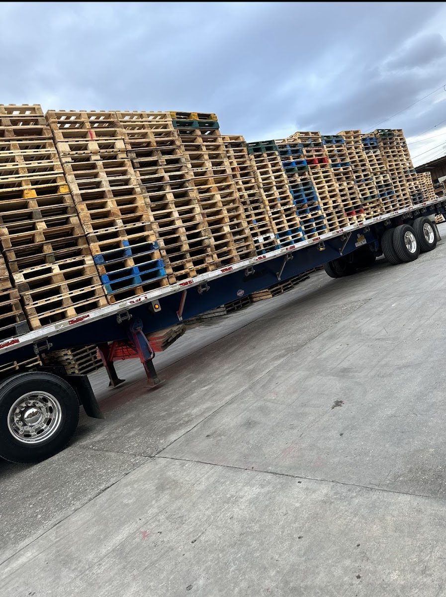 A flatbed trailer fully loaded and strapped with color-coded wood pallets ready for delivery